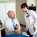 PAS faculty member holds a tube on a mannikin while a student in lab coat looks on